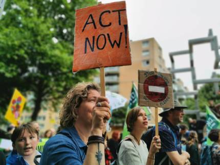 Op de Klimaatmars in Rotterdam houdt een vrouw een bord vast met de tekst act now.